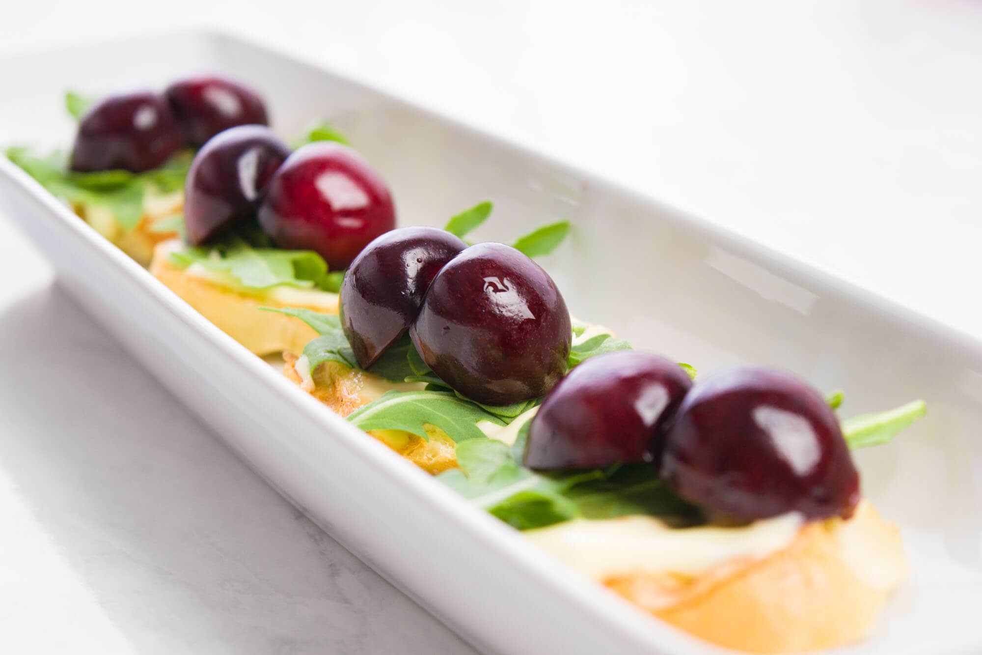Cherry and cheese appetizer with greens on a white platter for summer.