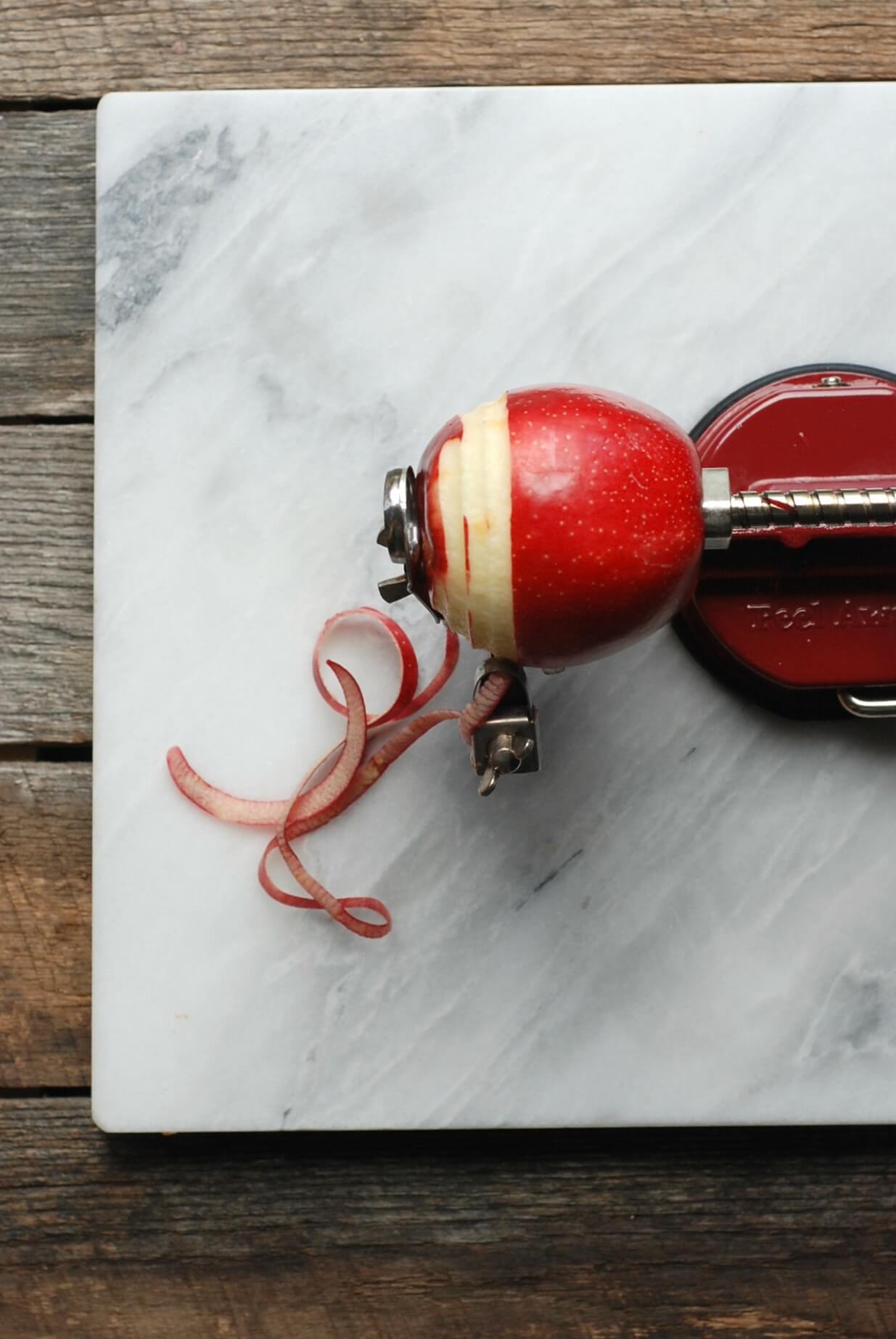 Apple peeler on marble surface with apple peel curls, used for freezing apples.