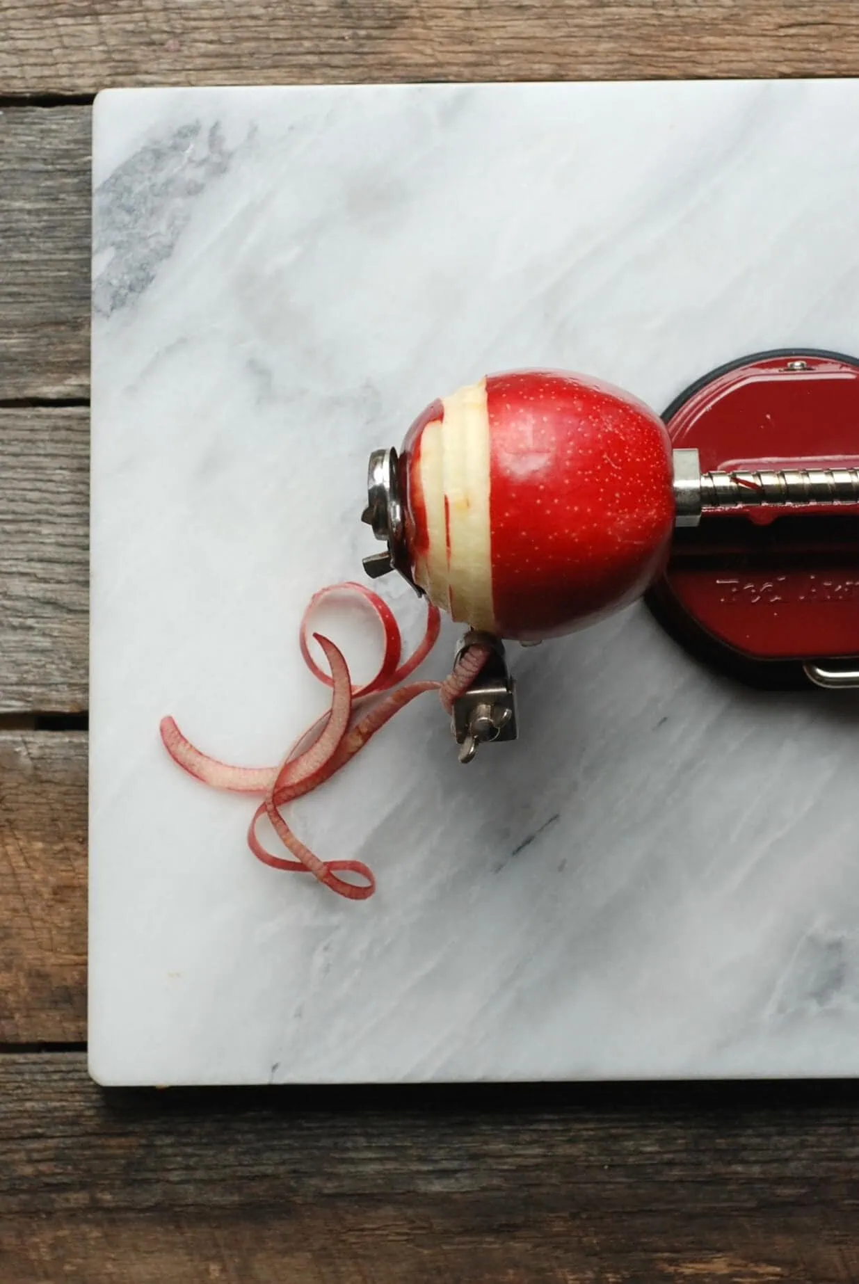 Apple peeler on marble surface with apple peel curls, used for freezing apples.