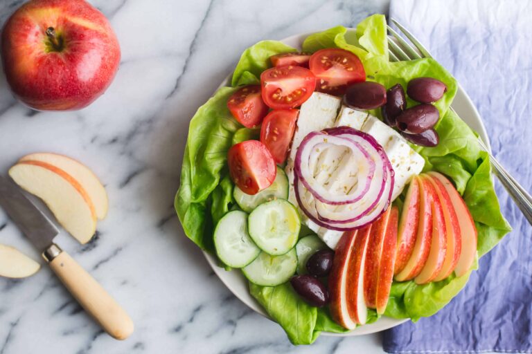 Fresh Greek salad with apples, tomatoes, cucumbers, olives, and feta cheese on a white plate.