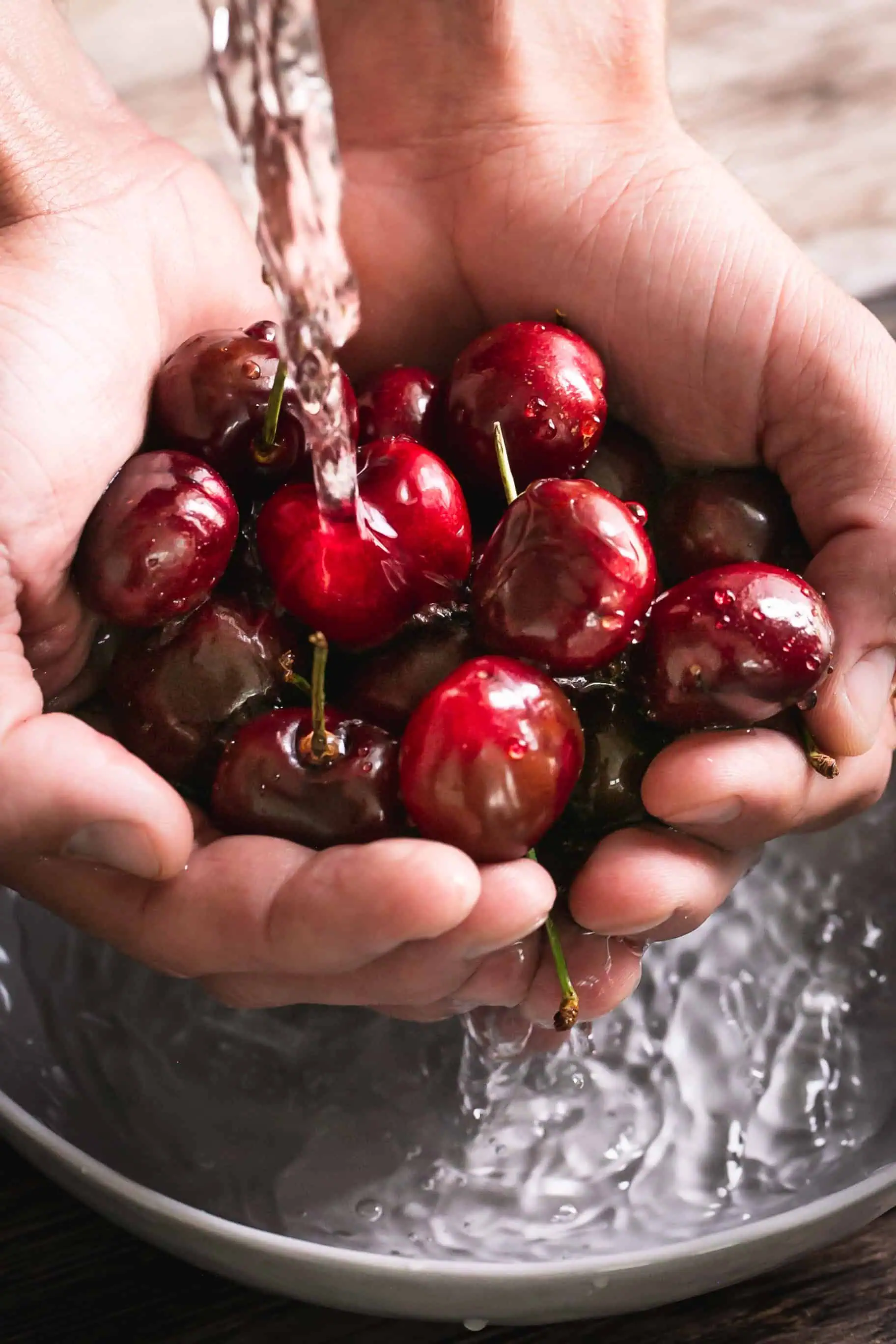 Fresh cherries being rinsed under water in a bowl for freezing.