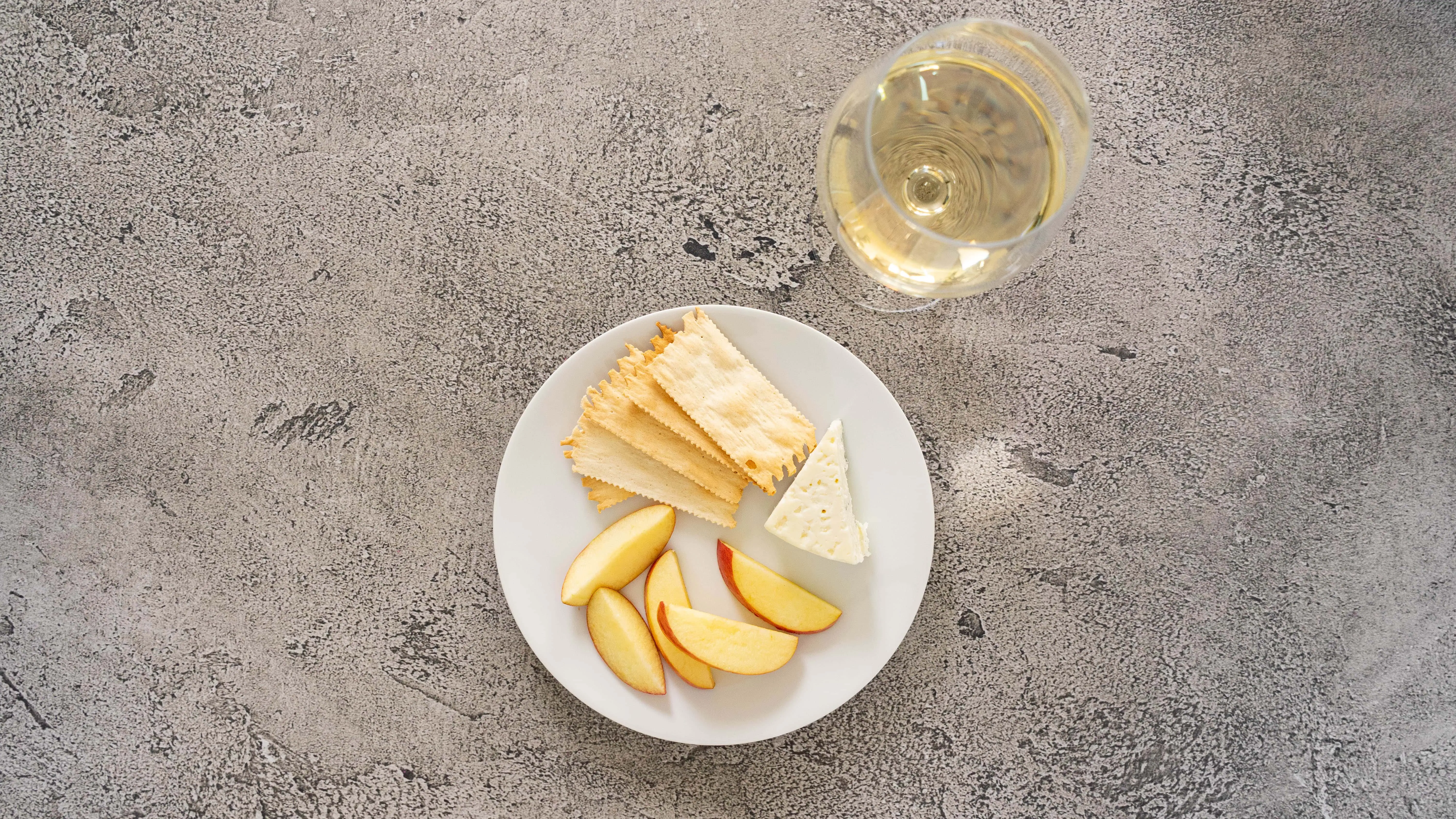 Fresh apple slices, cheese, and a glass of white wine on a gray surface.