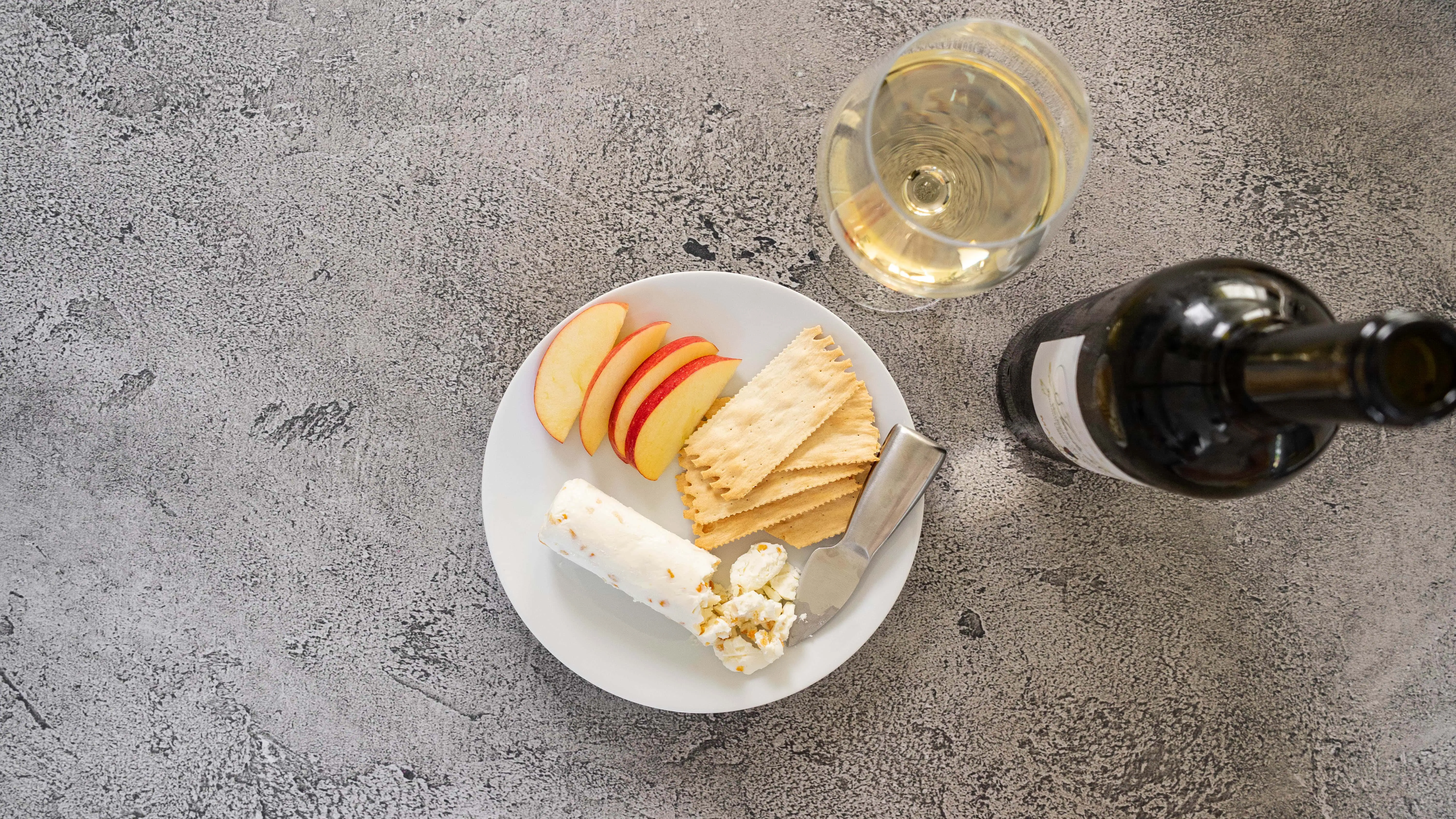 Apple slices, cheese, and a glass of white wine on a gray surface.