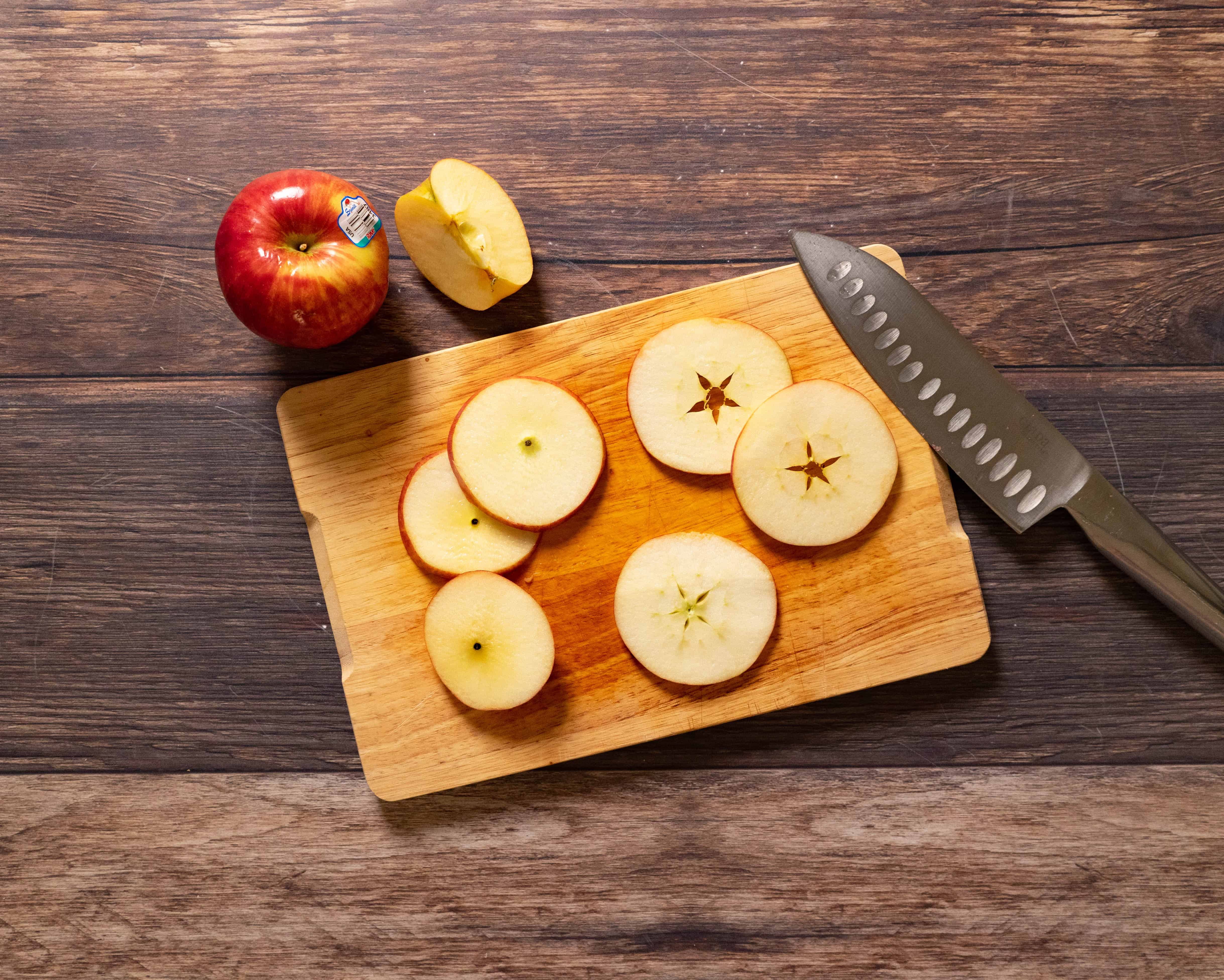 Sliced apples on a wooden cutting board with a knife and whole apple nearby.