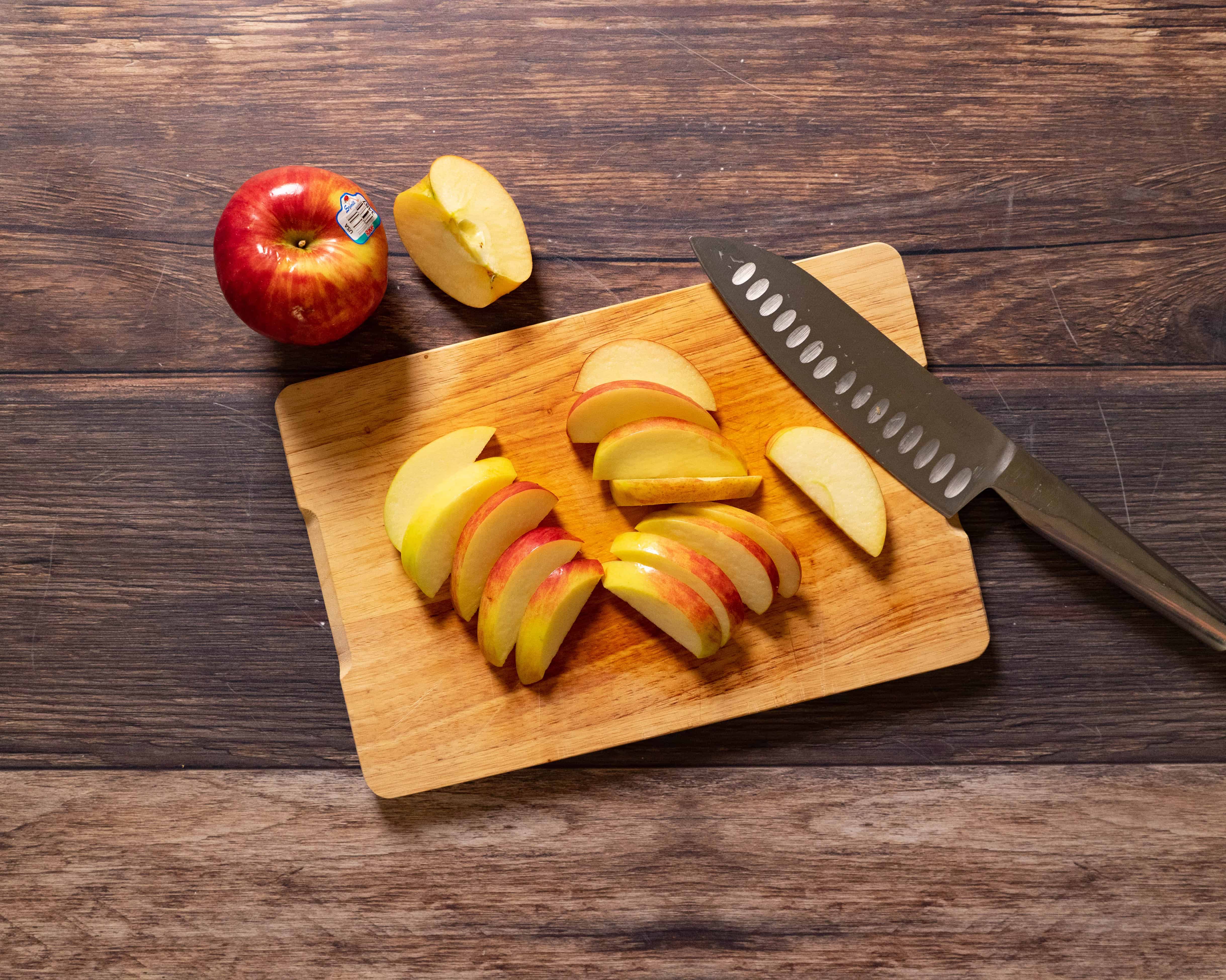 Sliced apples on a wooden cutting board with a knife and whole apple nearby.
