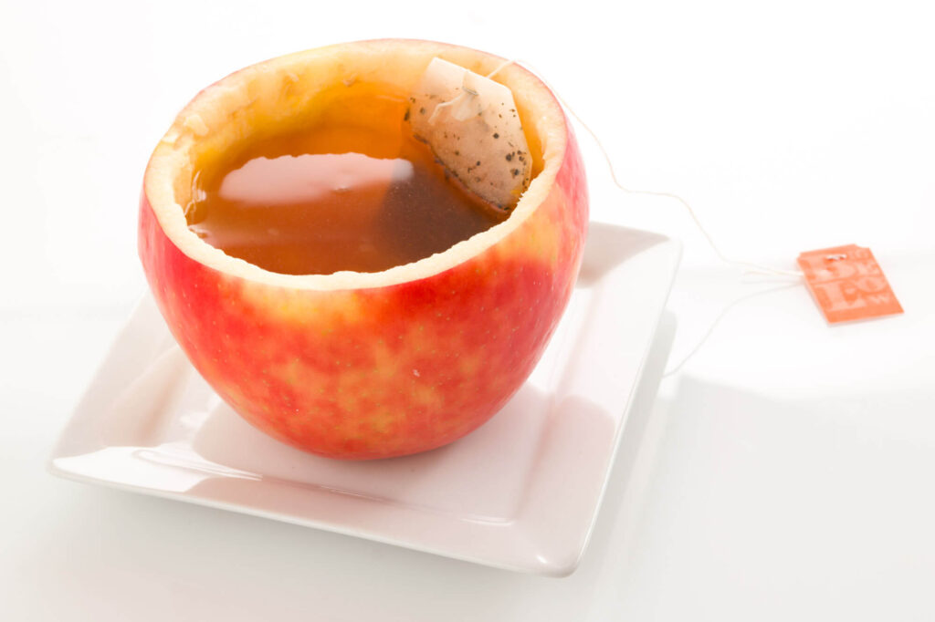 Apple filled with tea and a tea bag on a white plate.