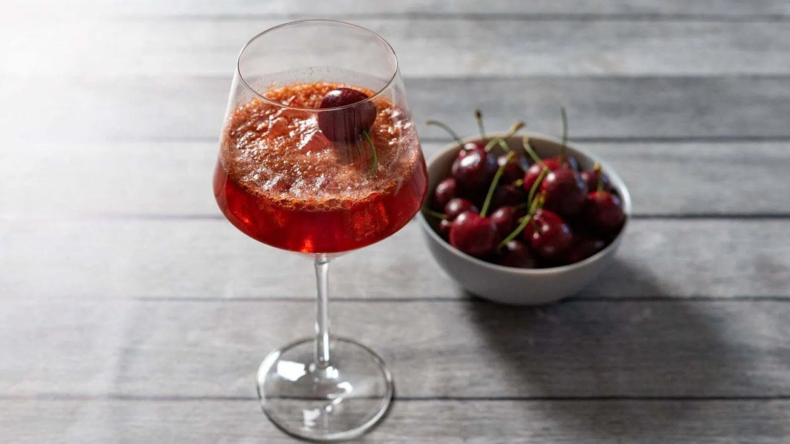 Cherry Spritz cocktail with fresh cherries on a wooden table.