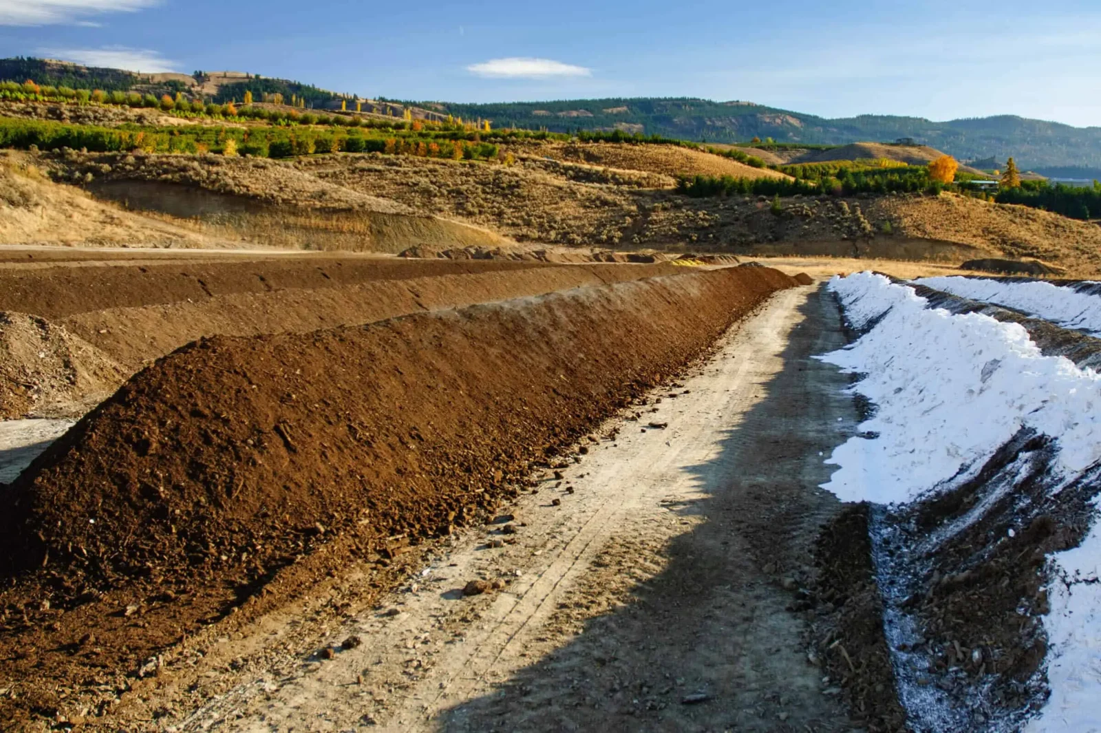 Vineyard soil preparation with rows of soil and snow in a hilly landscape.