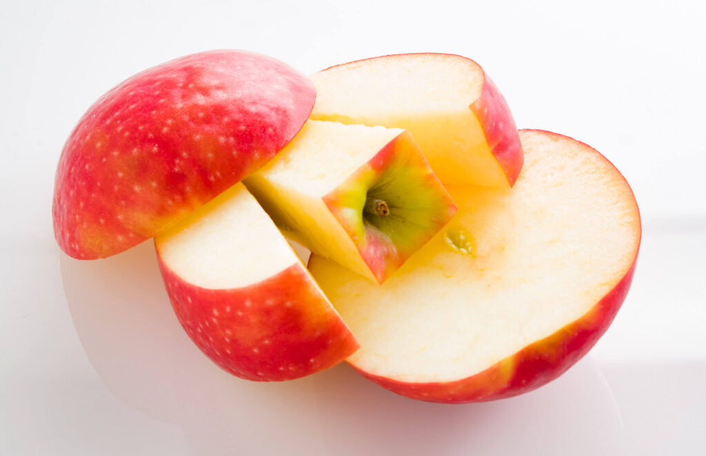 Fresh red apple with slices revealing yellow flesh on white background.
