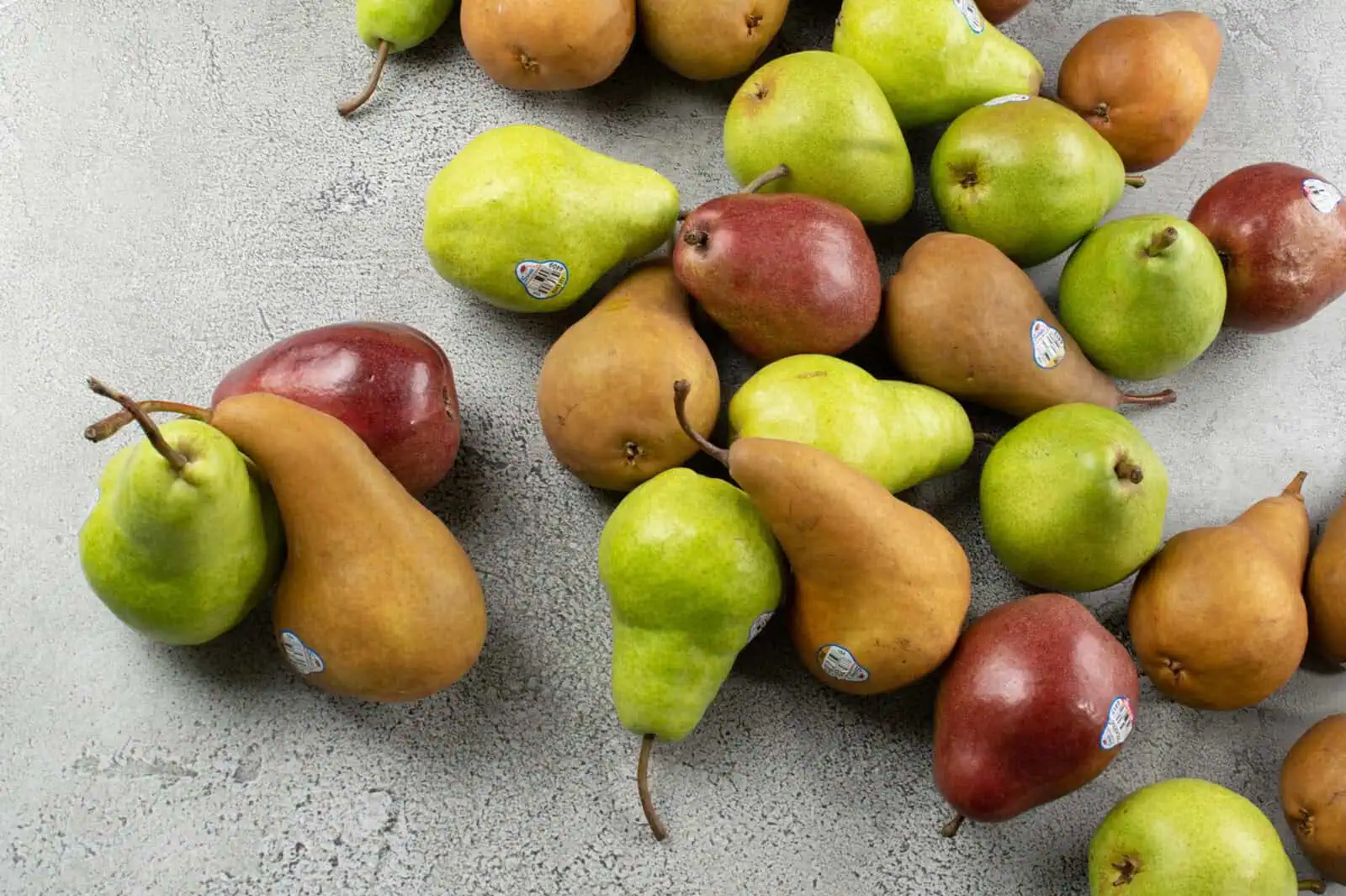 Assorted Rushing Rivers® Pears in green, red, and yellow on a gray surface.