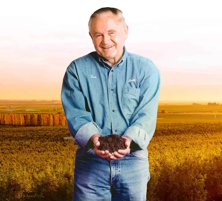Farmer holding soil in a field at sunset, promoting sustainable agriculture.