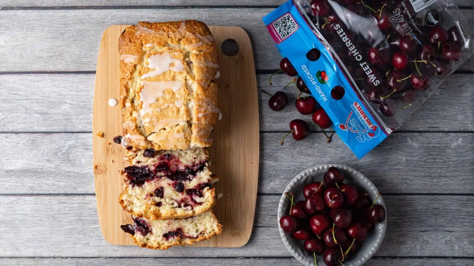Slice of cherry cake with fresh cherries on a wooden board and a bowl of cherries.