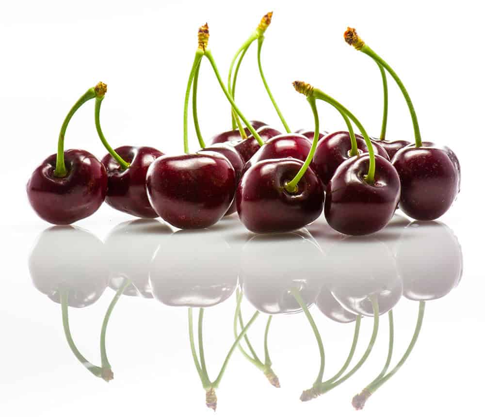 Fresh ripe Stemilt cherries with green stems on a white background.