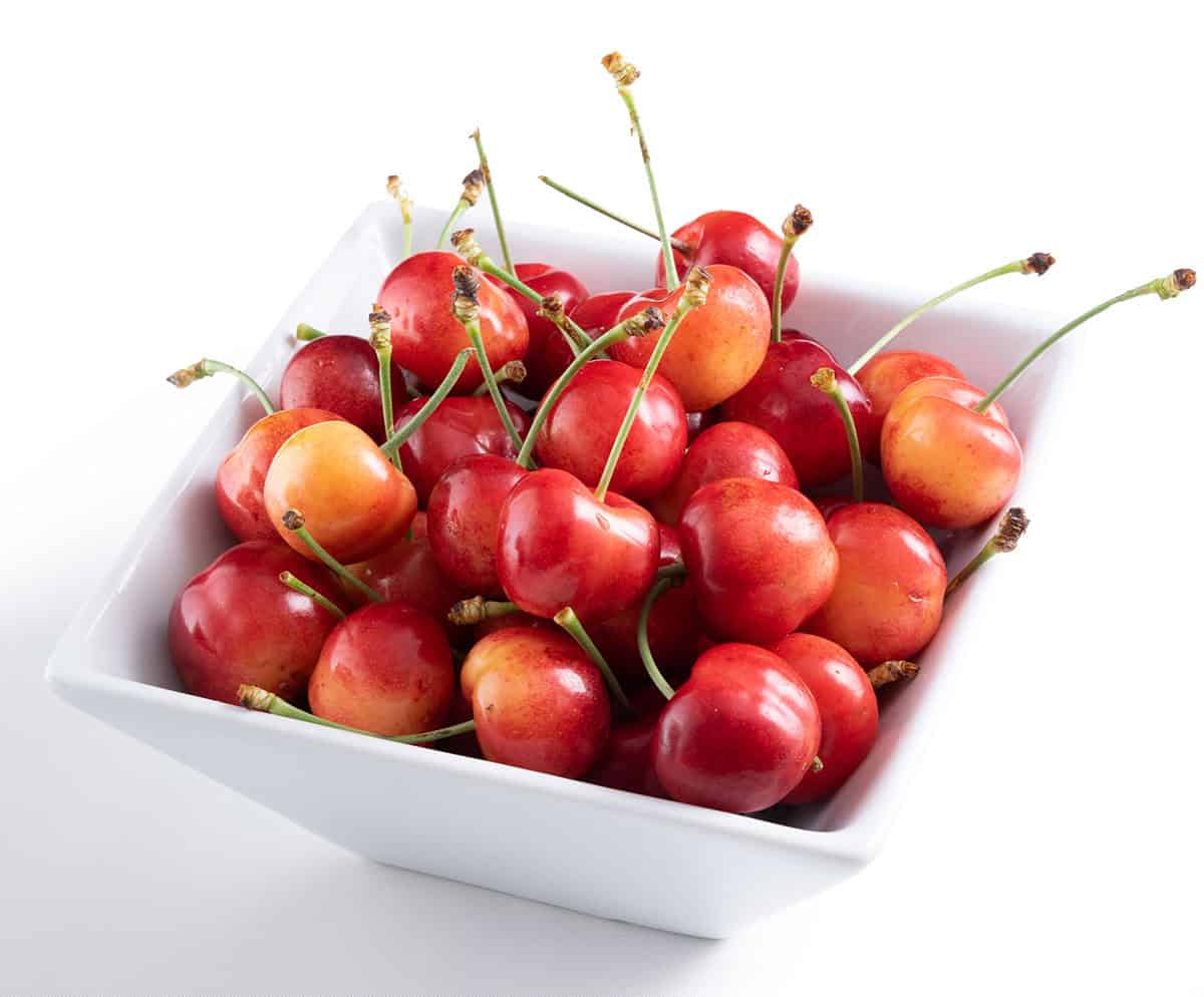 Fresh Skylar Rae&reg; cherries in a white bowl, vibrant and ripe for snacking.