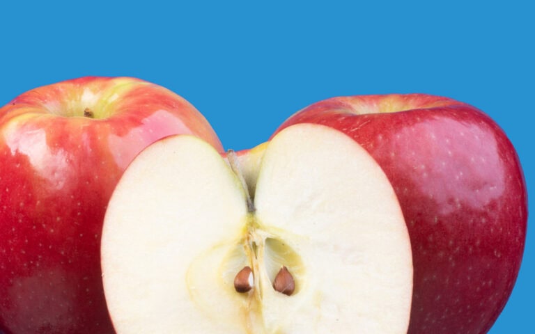 Fresh red apple cut in half showing seeds on a blue background.