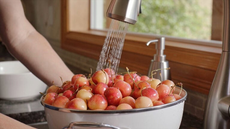 Person rinsing Skylar Rae&reg; cherries under running water in a bowl.
