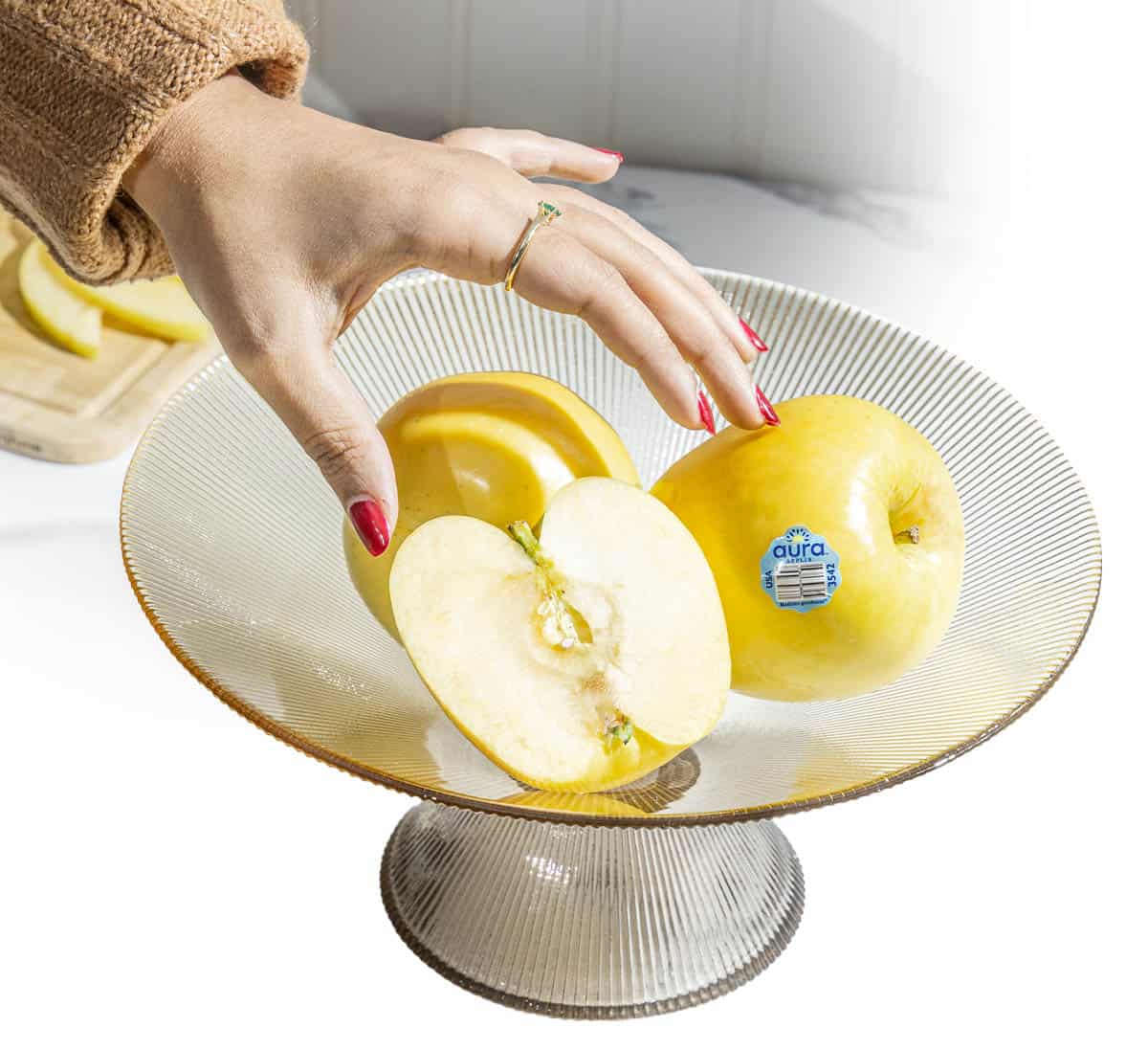 Fresh Aura&reg; apples on a glass cake stand with a hand reaching for one.