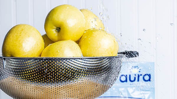 Fresh yellow apples in a metal bowl on a white wooden background.