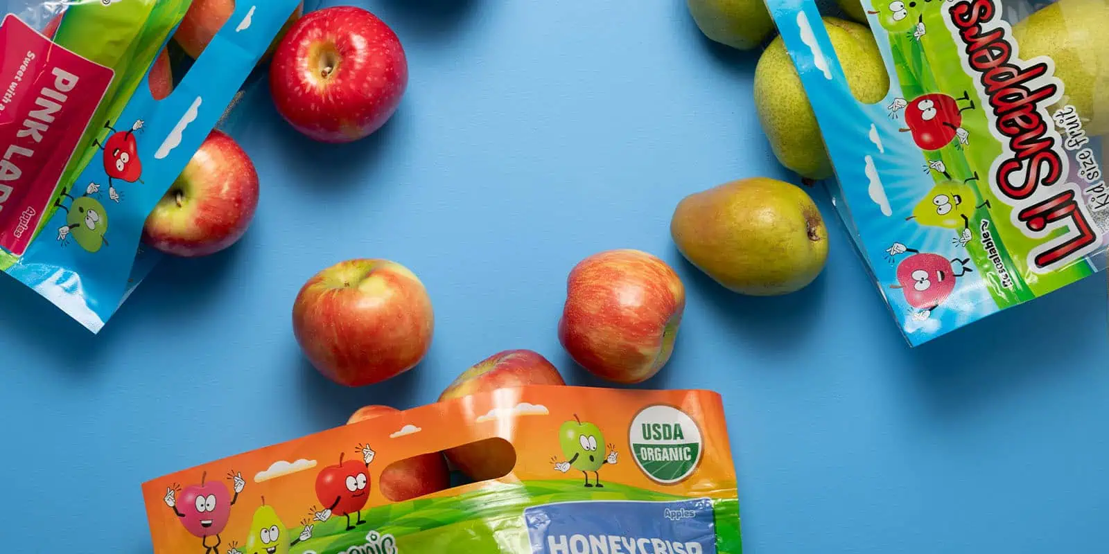 Fresh organic apples and pears with Stemilt Lil Snappers® packaging on blue background.